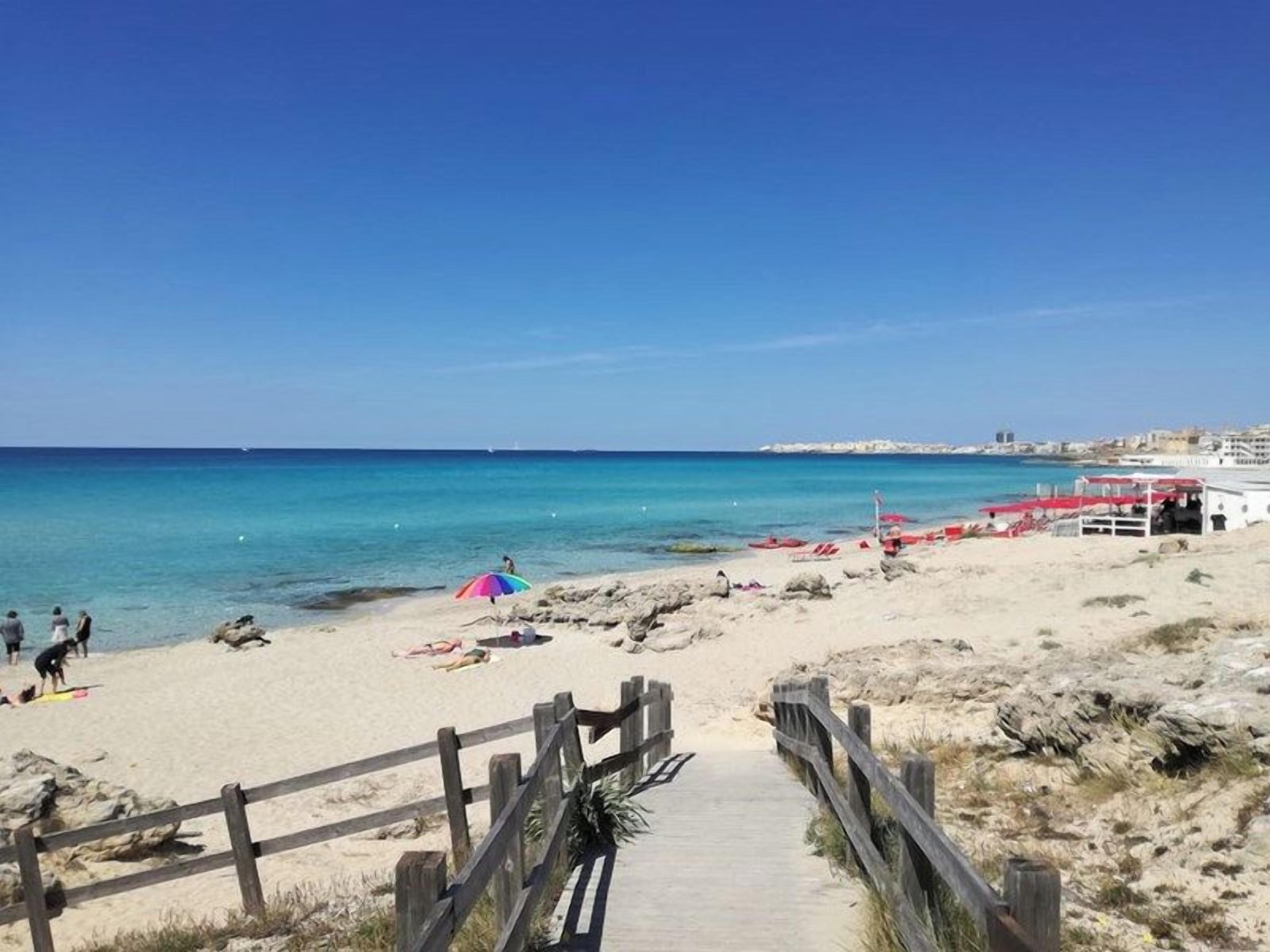 A beach with a wooden walkway leading to the shore, a few people, and beach umbrellas.