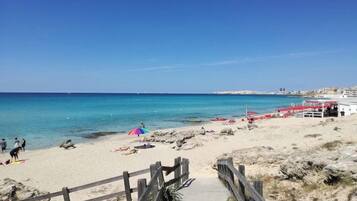 Ein Strand mit einer Holzpromenade, die zum Ufer führt, ein paar Personen und Strandsonnenschirme.