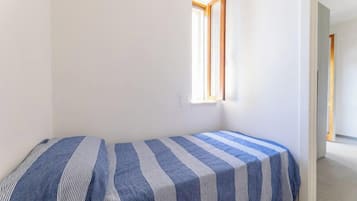 Acomodação pequena, com um quarto único, duas camas, uma janela e porta que dá para outro espaço.