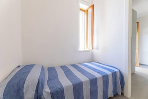 Eine kleine, einfache Unterkunft mit zwei Betten, einem Fenster und einer Tür zu einem anderen Raum.