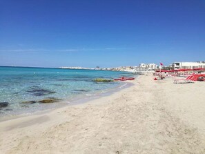 Een strand met helder turquoise water, een zandstrand en rode strandparasols.