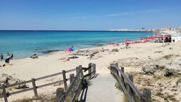 Une plage avec une promenade en bois menant au bord de l’eau, quelques personnes et des parasols de plage.