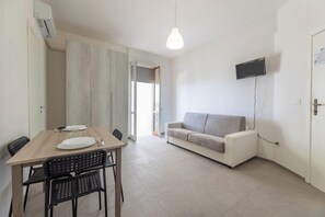 Un espace de vie compact comprenant un coin repas, un canapé et un téléviseur fixé au mur.