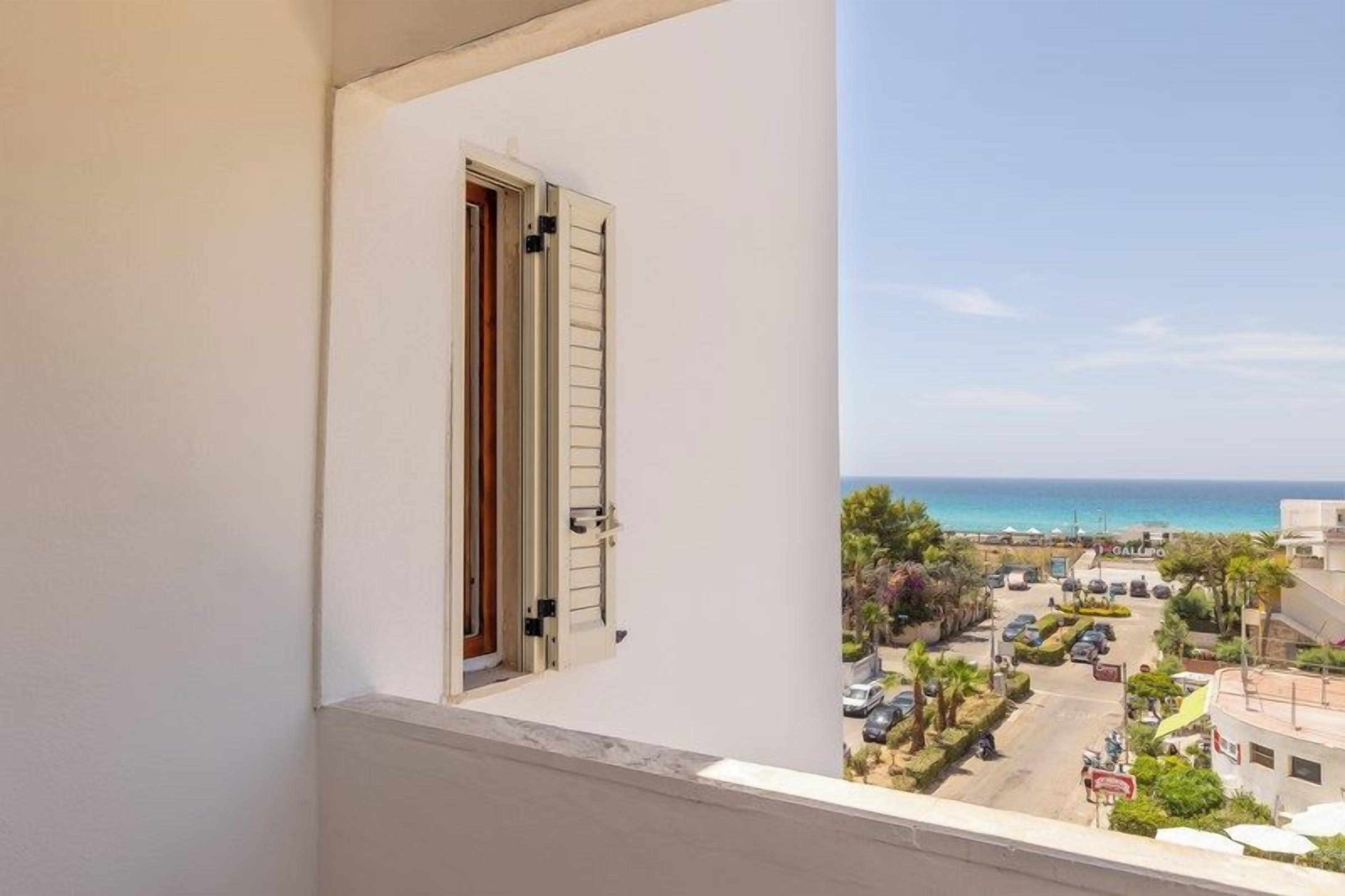 A balcony with a view of the sea and a parking area.