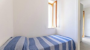 Un petit logement composé d’une seule pièce, avec deux lits, une fenêtre et une porte donnant sur une autre pièce.