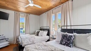 Ein Hotelzimmer mit zwei Betten, einem Deckenventilator und einem an der Wand montierten Fernseher.