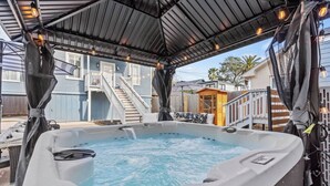 Ein Whirlpool mit überdachter Terrasse, eine Treppe zu einer Holzterrasse und eine kleine Holzhütte.