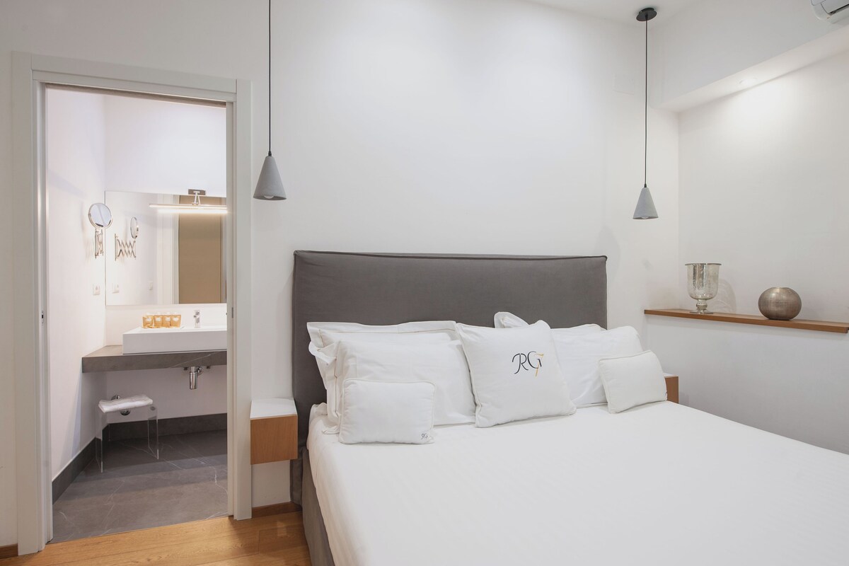 A bedroom with a bed, bedside tables, a mirror, and a shelf with a glass and a decorative item.