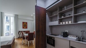 A compact hotel room with a bed, a dining table with chairs, a kitchenette with a sink, and a view of the outside through a window. - Rg7 Apartments (Catania)