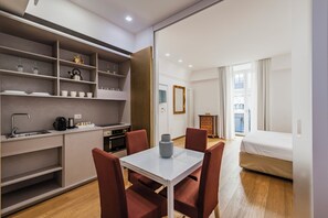 A compact hotel room with a kitchenette, a dining area with a table and chairs, a bed, and a view of the city through large windows. - Rg7 Apartments (Catania)