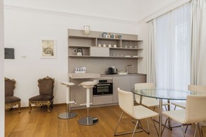 A modern kitchen with a glass dining table and bar stools, a coffee machine, and a built-in oven.