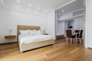 A modern hotel room with a large bed, a bedside table, a chair, and a small table with a chair. - Rg7 Apartments (Catania)