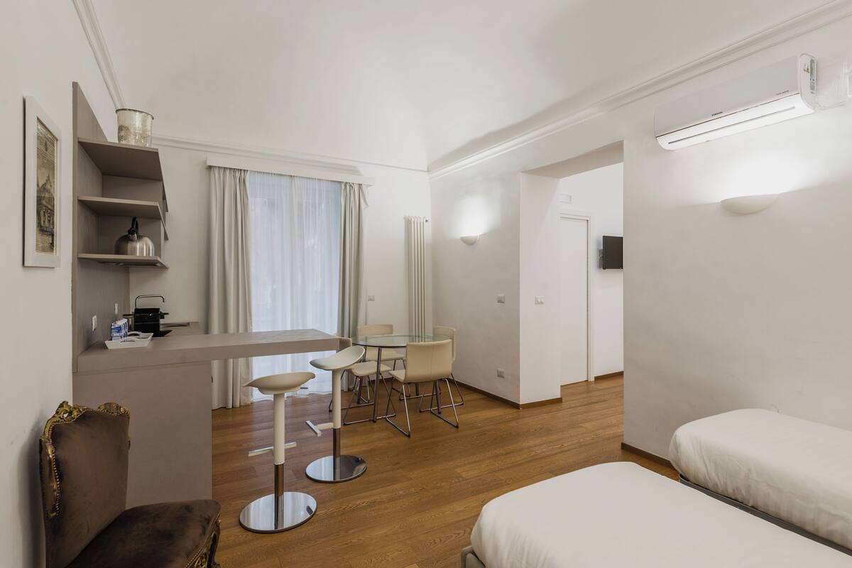 Una habitación de hotel moderna con comedor, cama, sillón y televisor.