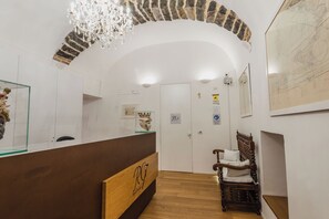 A reception area with a wooden reception desk, a chandelier, a stone arch, and a wooden chair.