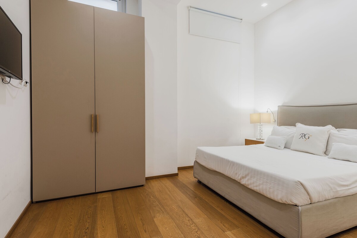 A bedroom with a bed, a wardrobe, a nightstand, and a wall-mounted TV.