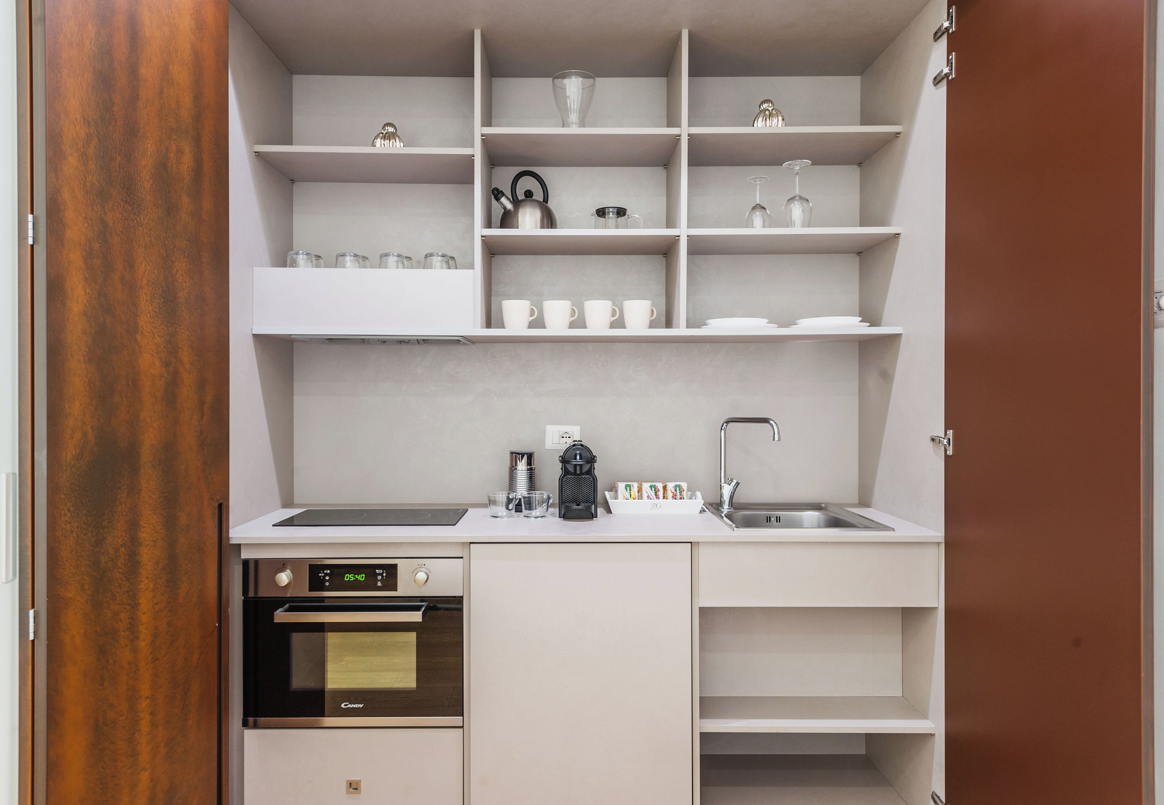 A compact kitchen with white cabinetry, a built-in oven, a coffee maker, and a sink.