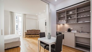 A compact living space with a bed, a dining table with chairs, a kitchenette, and a sofa. - Rg7 Apartments (Catania)