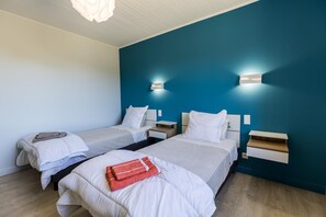 Habitación de hotel con dos camas individuales, suelo de madera y una pared de acento azul.