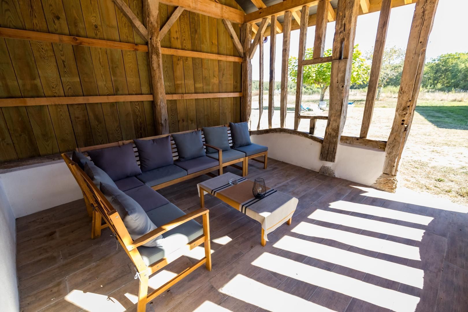 A covered outdoor seating area with a wooden bench and a sofa.