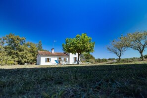 Una casa blanca con techo de tejas, un árbol en primer plano y un cielo azul despejado.