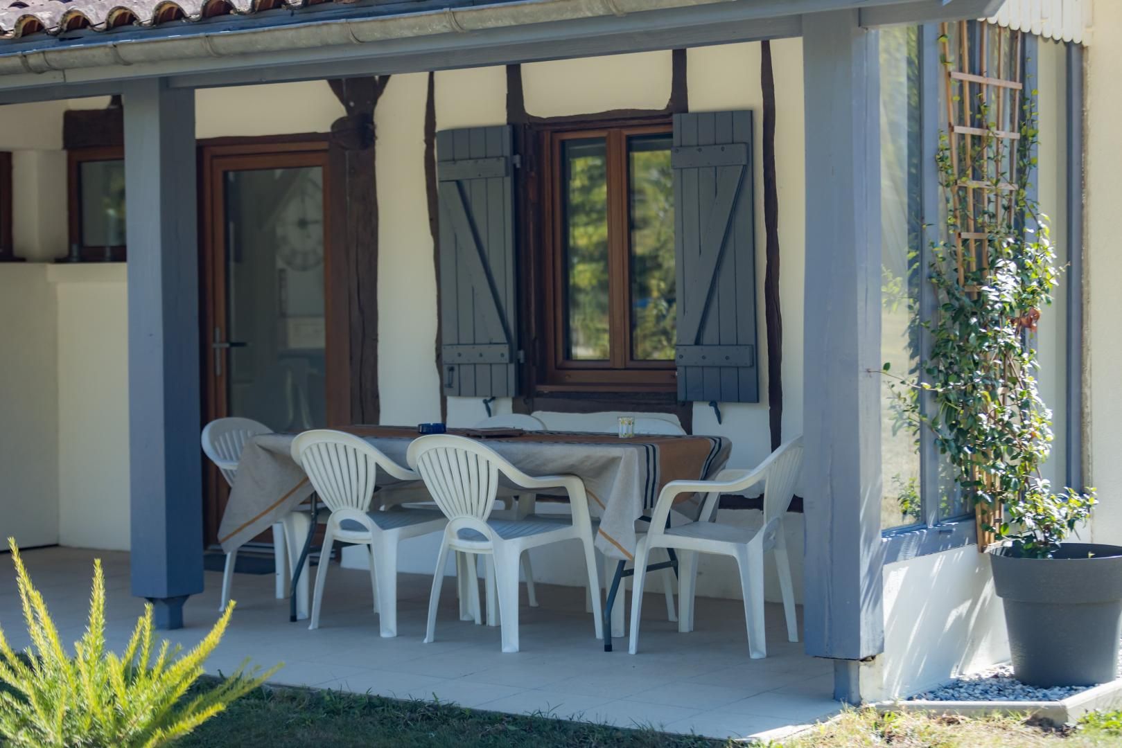 An outdoor patio with a table and chairs, a potted plant, and a window with shutters.