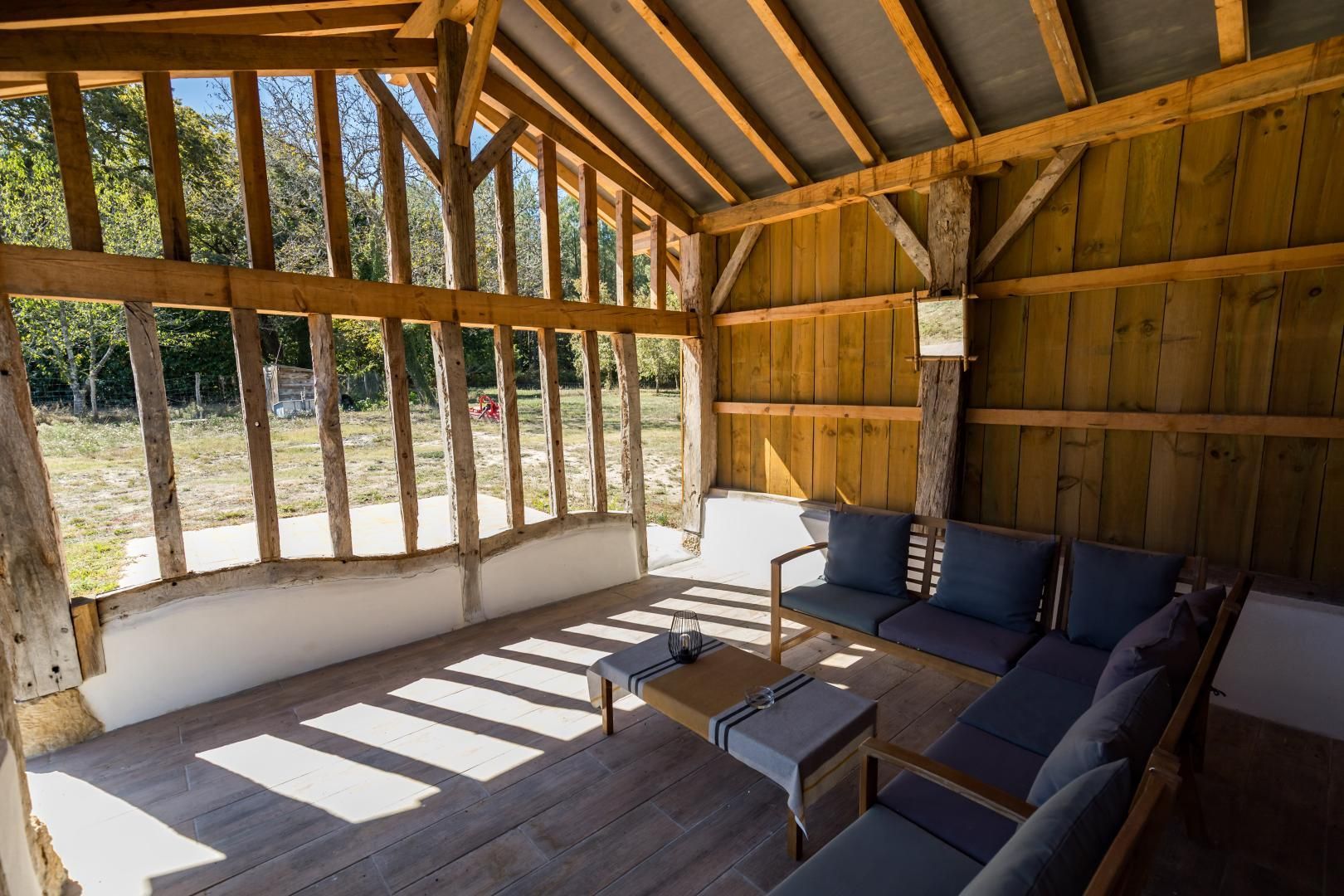 A covered outdoor seating area with a wooden ceiling and walls, a sofa, and a small table.