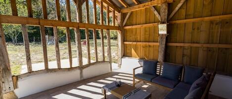 A covered outdoor seating area with a wooden ceiling and walls, a sofa, and a small table.
