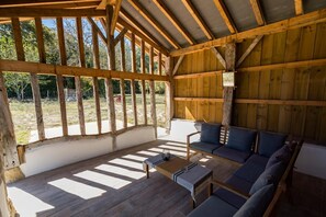 A covered outdoor seating area with a wooden ceiling and walls, a sofa, and a small table. - Gîte du Marsaou - MAILLERES (MAILLERES)