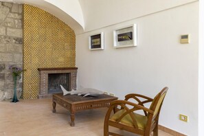 Una habitación con chimenea, una mesa de madera y una silla. Hay dos cuadros en la pared.