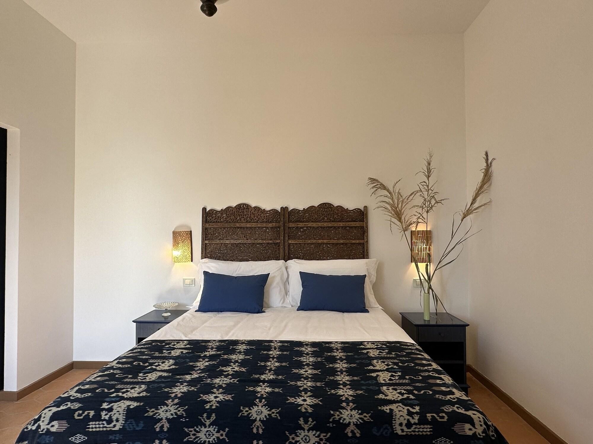 A bedroom with a large bed, two bedside tables, a decorative headboard, and a wall-mounted lamp.