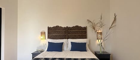 A bedroom with a large bed, two bedside tables, a decorative headboard, and a wall-mounted lamp.