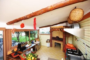 Une cuisine équipée d’une cuisinière à gaz, d’un four en briques et d’un coin repas avec une table et des chaises.