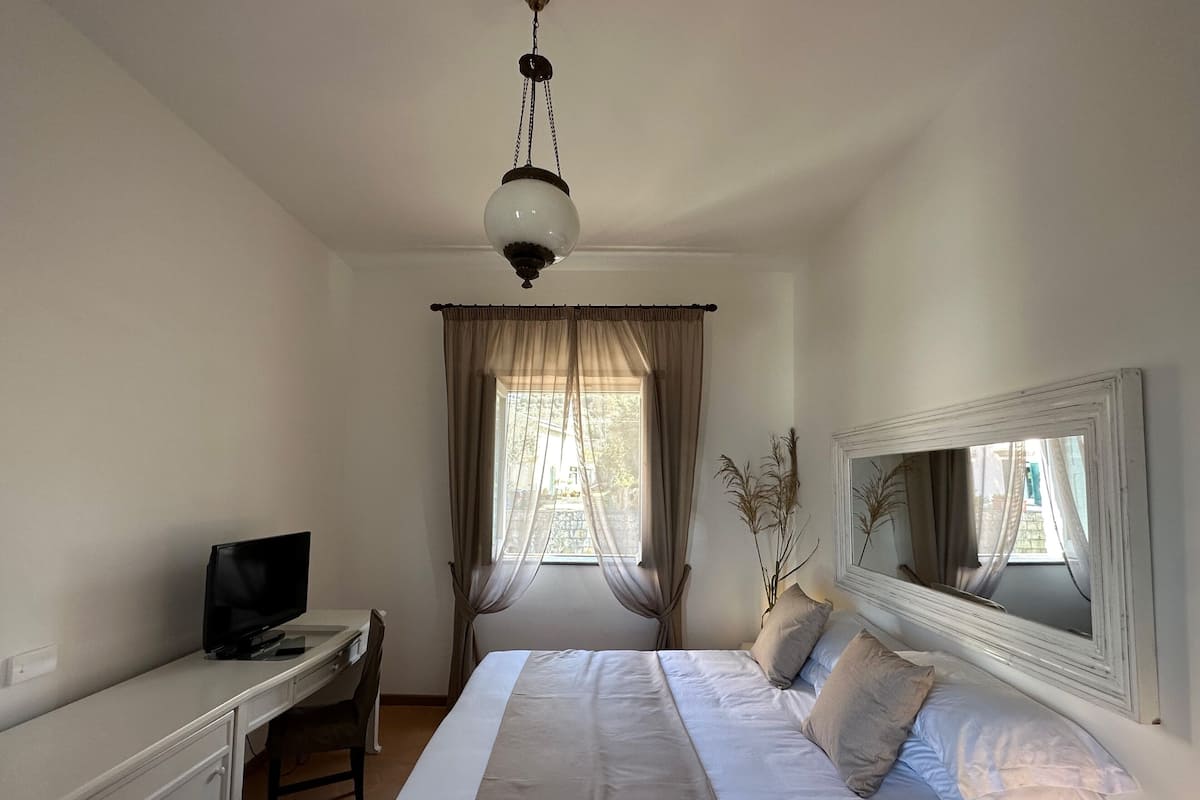 Une chambre à coucher comprenant un lit, un bureau, une télévision, une fenêtre avec des rideaux et un miroir.