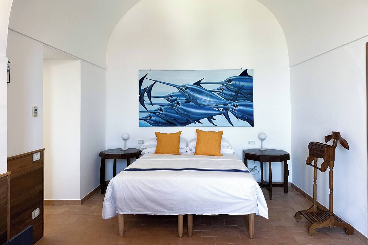 Une chambre avec un grand lit, deux tables de chevet, un plancher en bois et un tableau au mur.