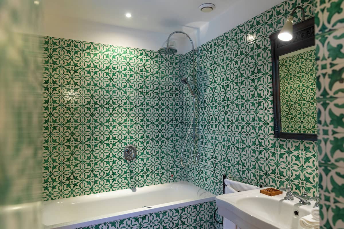 Une salle de bain avec une baignoire blanche, un lavabo et une douche. Les murs sont recouverts de carreaux verts et blancs à motifs.