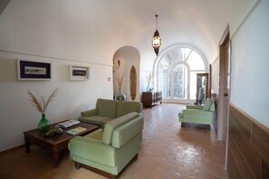 A spacious hallway with a high ceiling, green upholstered sofas, a wooden coffee table, and a hanging lantern. - Villa Puolo - With Private Sea Access (Sorrento)