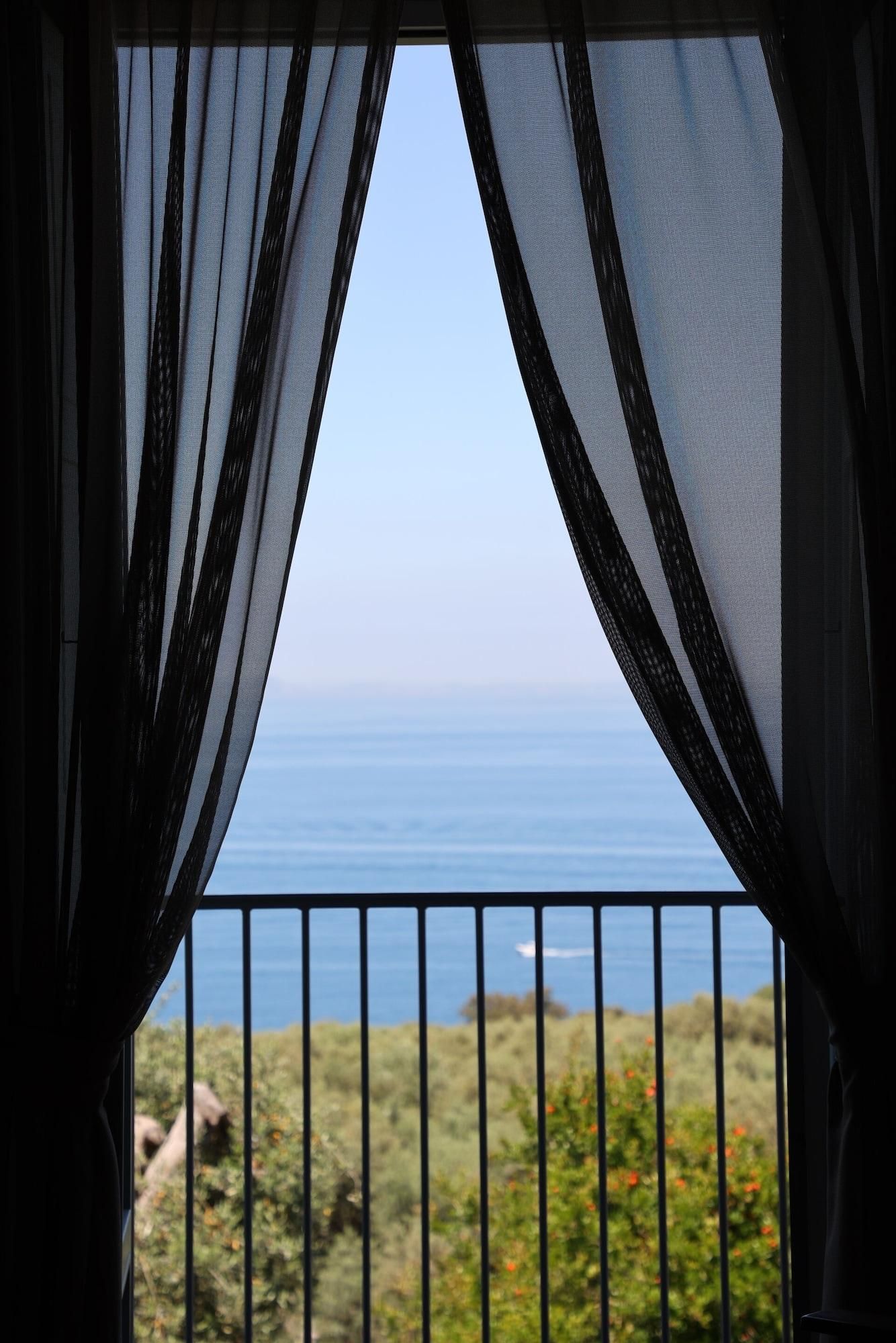 Blick durch transparente Vorhänge auf das Meer, im Vordergrund ein Geländer.