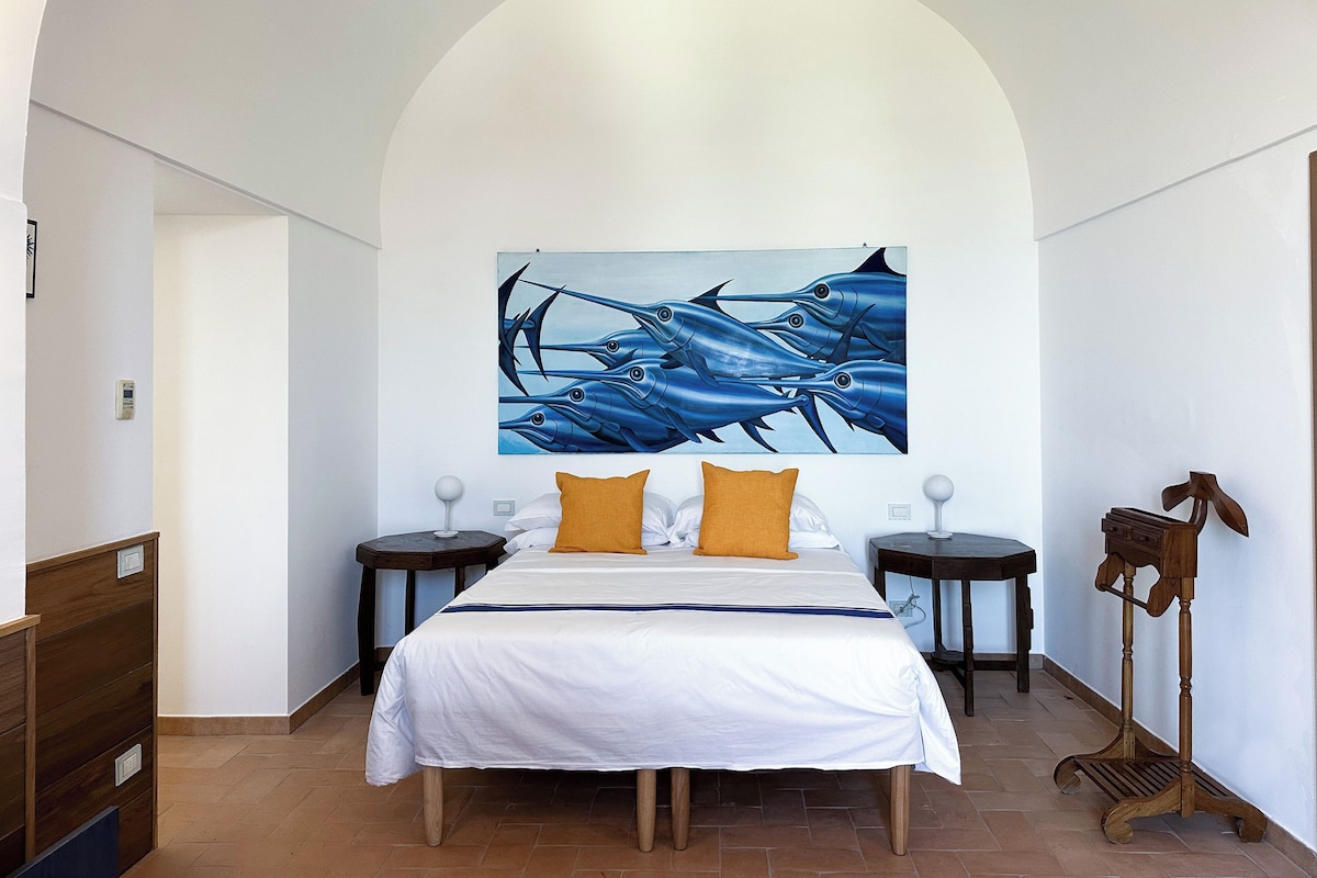 A bedroom with a large bed, two bedside tables, a wooden floor, and a painting on the wall.