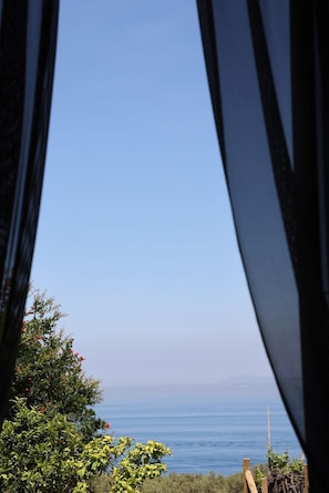 A view through window curtains of a coastal landscape with a clear sky, a body of water, and distant land.