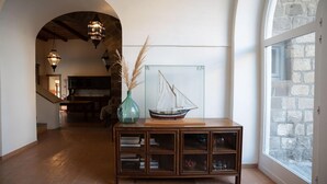Une console en bois surmontée d’une vitrine en verre contenant un modèle de bateau, un vase avec des plumes d’herbe des pampas et un petit meuble renfermant des livres et des objets décoratifs.