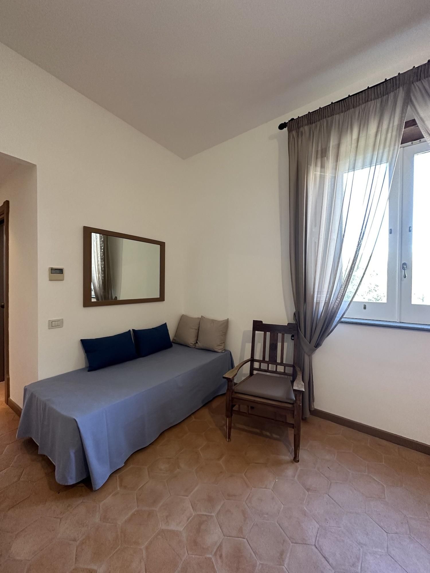 Une pièce comprenant un lit, une chaise, une fenêtre avec des rideaux, un miroir fixé au mur et un thermostat.