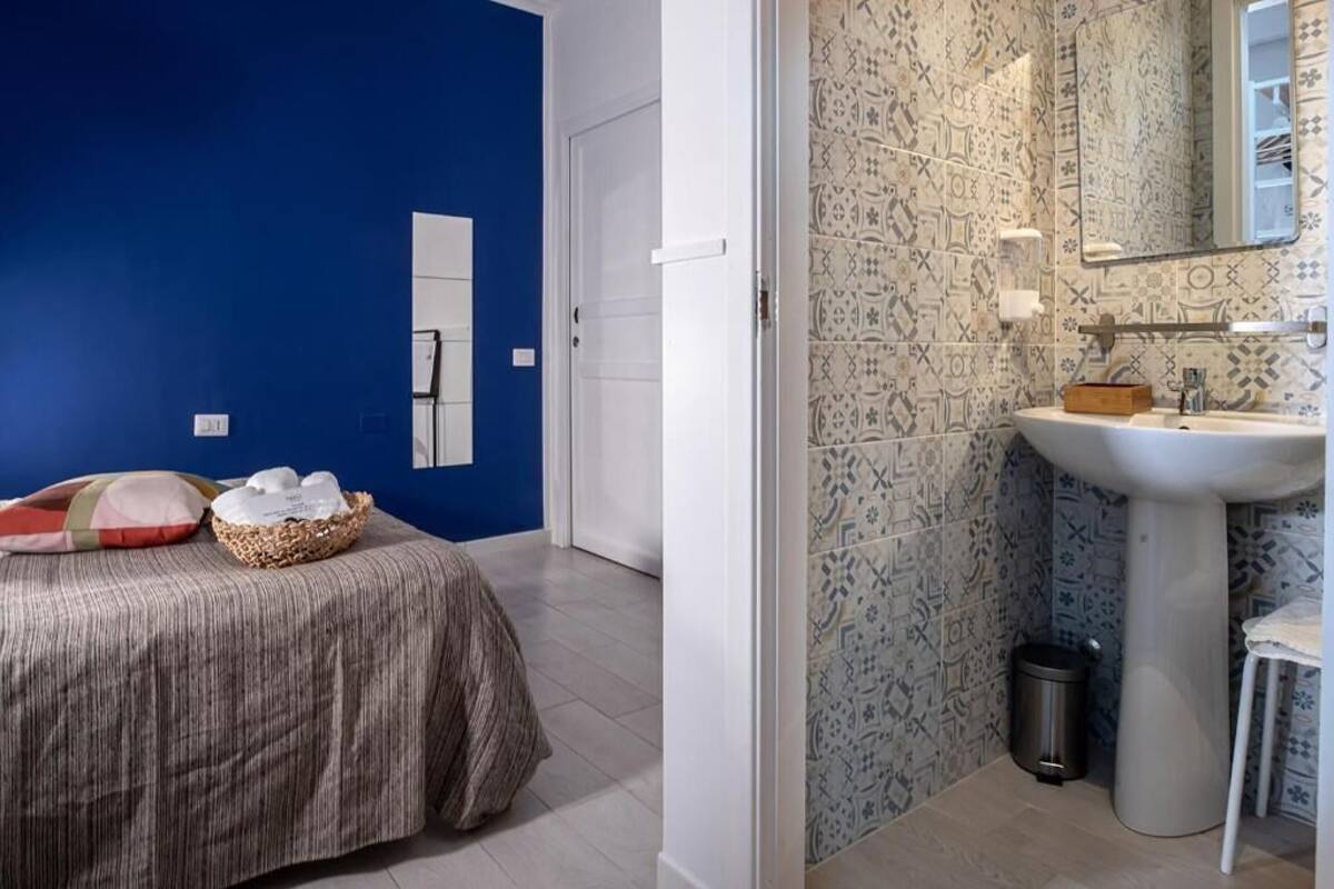 A bedroom with a bed, a bedside table with a basket, and a blue wall.