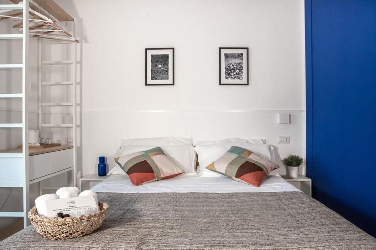 A bedroom with a bed, pillows, a basket, and two framed pictures on the wall.