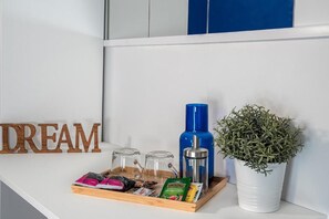 Un comptoir blanc sur lequel se trouve un plateau en bois contenant des en-cas, une bouteille bleue, un récipient en métal et une plante en pot.
