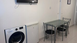 Un espacio habitable pequeño con lavadora, una mesa con sillas y un televisor montado.