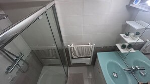 Un baño moderno con cabina de ducha de vidrio, un lavabo con espejo y un estante con artículos de aseo.