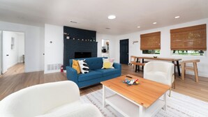 A modern living room with a blue sofa, white armchairs, a wooden coffee table, and a fireplace.