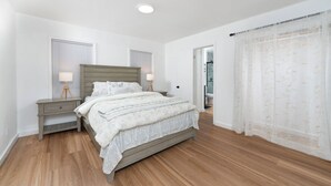 A bedroom with a bed, two bedside tables, a window, and a door leading to a bathroom.