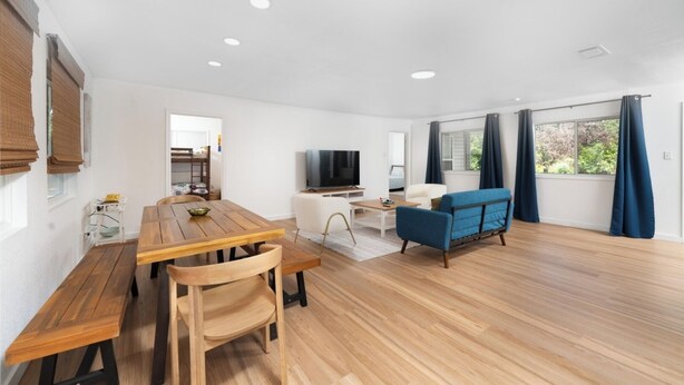 A modern living room with a wooden dining table, a blue sofa, a TV, and a window with curtains.