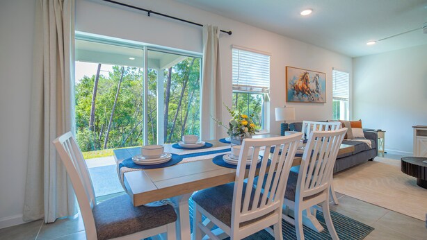 A dining area with a table set for four, white chairs, a vase with flowers, and a painting on the wall. - Escape the Winter! Cozy 3BR Retreat in Sunny Ocala, Florida (Ocala)